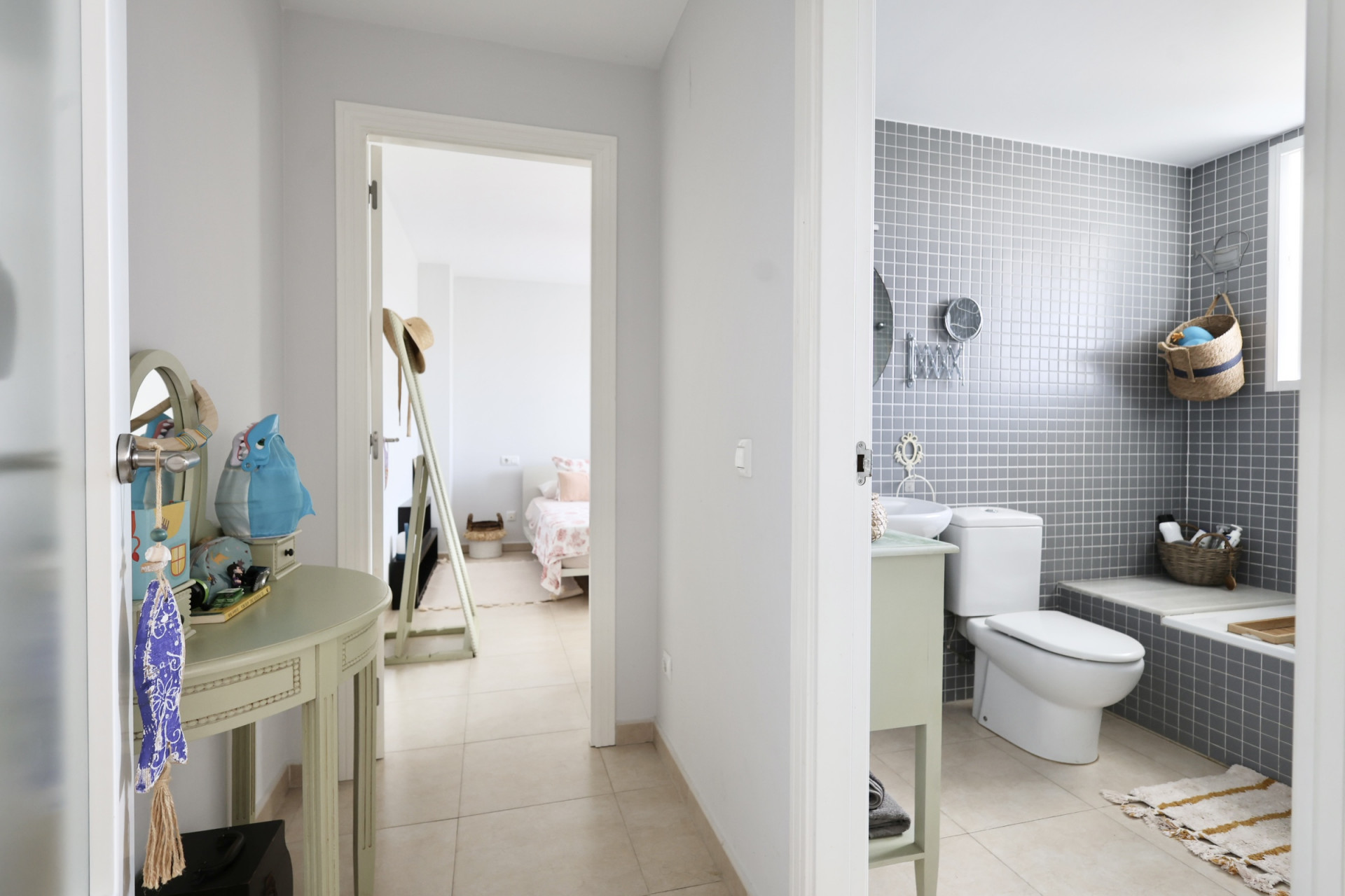 Detalle del pasillo con consola decorativa y vista al baño con azulejos grises y dormitorio al fondo.