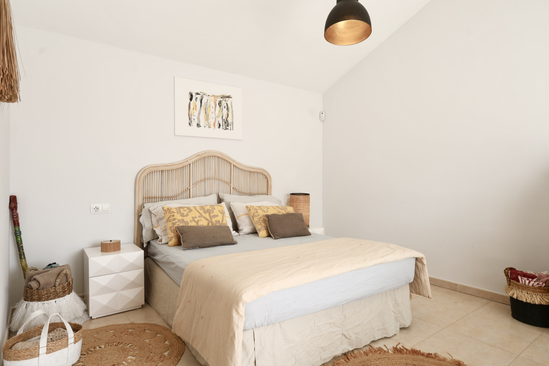 Habitación luminosa con cama de ratán, alfombra de yute redonda y decoración minimalista.
