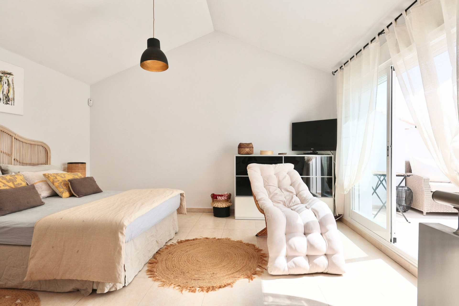 Luminoso dormitorio con cama de ratán, alfombra de yute y acceso a terraza.