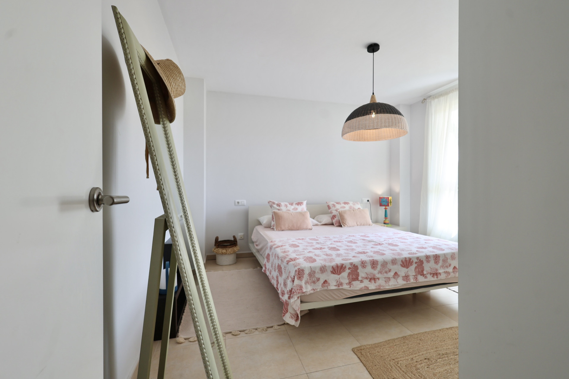 Luminoso dormitorio con cama doble, ropa de cama con motivos marinos y lámpara colgante de mimbre.