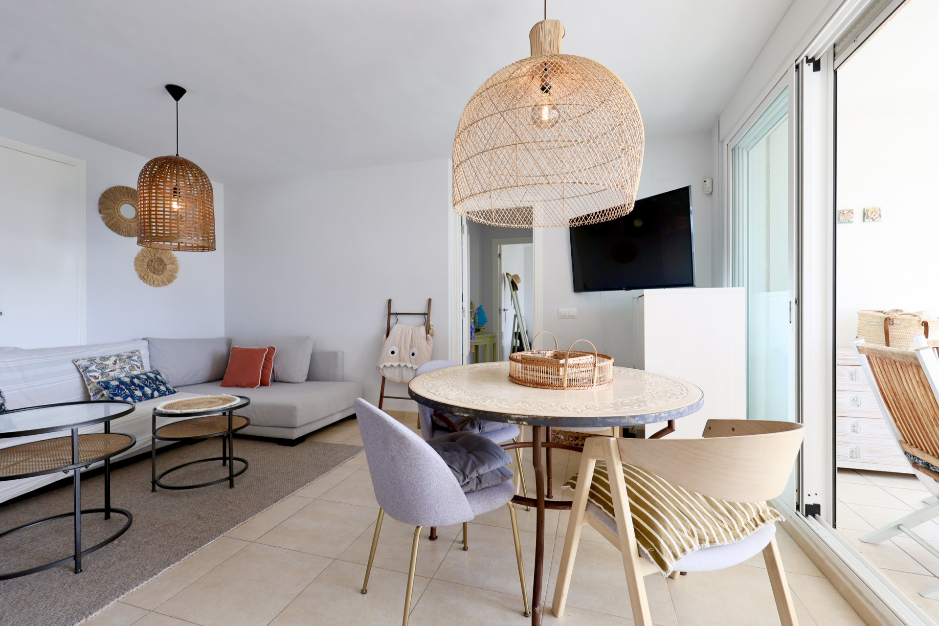 Salón comedor luminoso con lámparas de mimbre y acceso a la terraza.