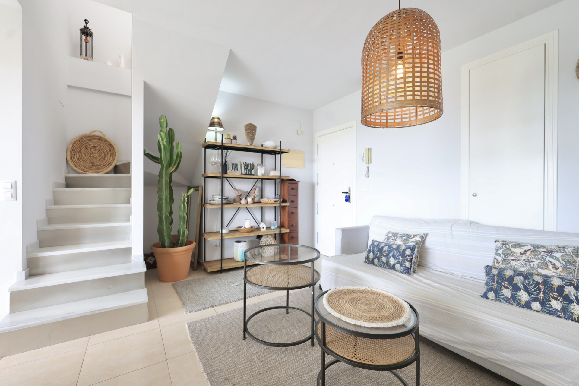 Salón luminoso con escalera de acceso al dúplex, decoración minimalista y lámpara colgante de mimbre.
