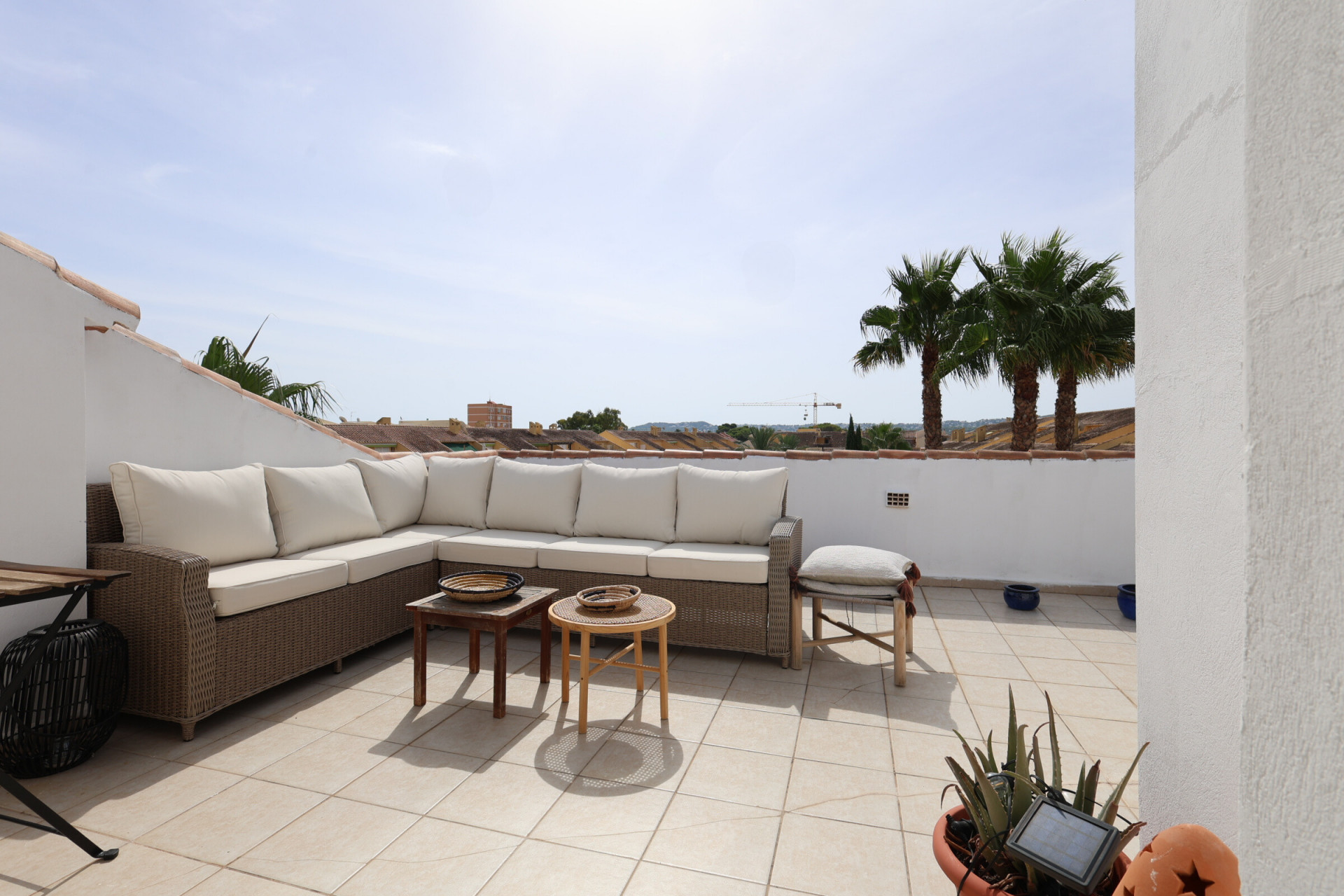 Soleada terraza con baldosas, sofá esquinero de mimbre y vistas a las palmeras.