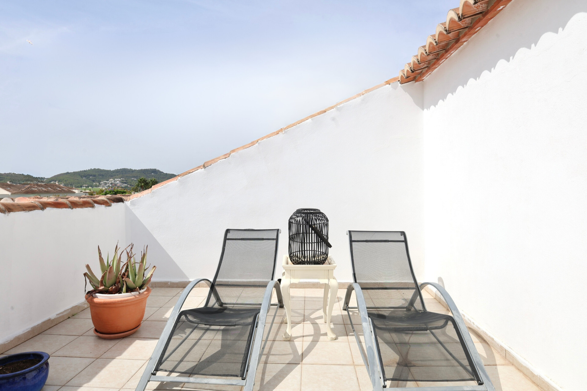 Terraza con dos tumbonas de metal, mesa auxiliar y vistas a la montaña.