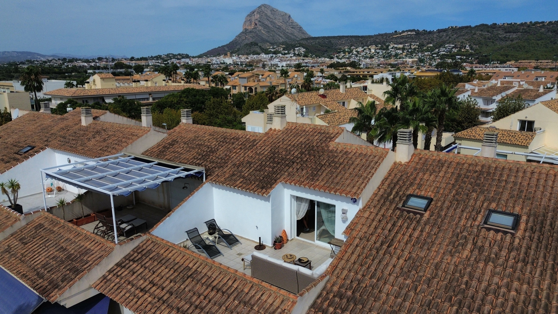 Vista aérea de la terraza solárium con toldo y mobiliario exterior, rodeada de tejados de teja.