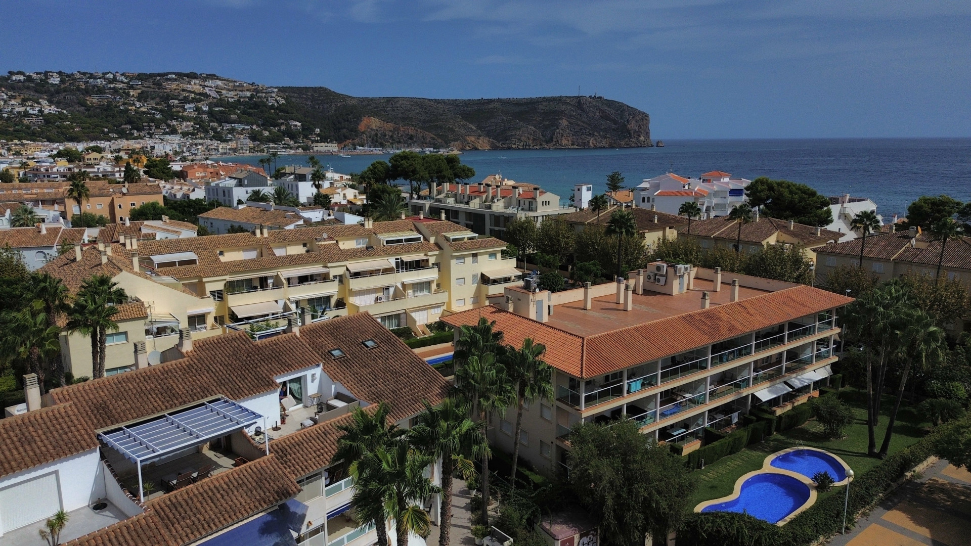 Vista aérea de la urbanización con piscina y edificios residenciales de tejas rojas cerca de la costa de Jávea.