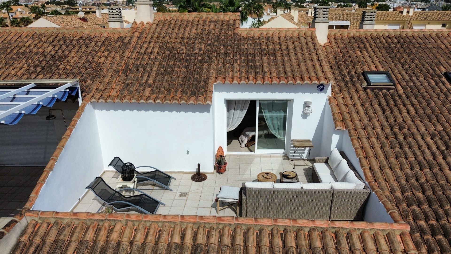 Vista elevada de la terraza con solárium, mobiliario de exterior y acceso al interior.