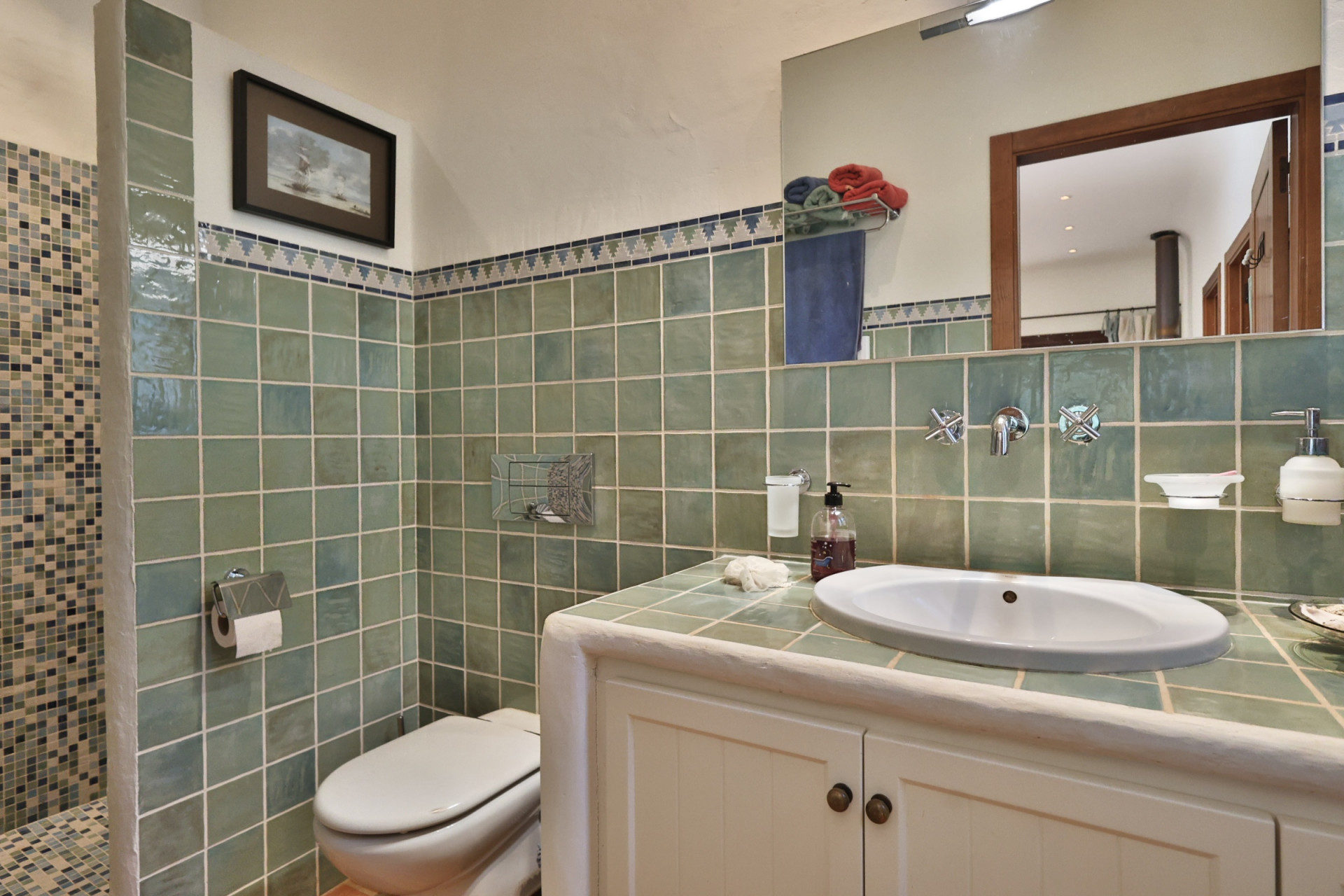 Baño funcional con paredes de azulejos verdes, lavabo integrado en mueble blanco y ducha con mosaicos azules y blancos. Baño funcional con paredes de azulejos verdes, lavabo integrado en mueble blanco y ducha con mosaicos azules y blancos.