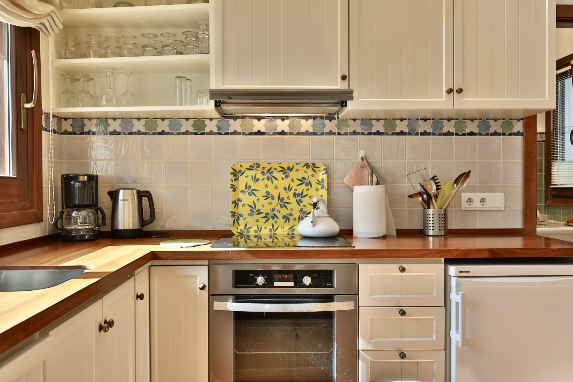 Cocina con encimera de madera y armarios crema, destacando un horno integrado y azulejos con cenefa decorativa. Cocina con encimera de madera y armarios crema, destacando un horno integrado y azulejos con cenefa decorativa.
