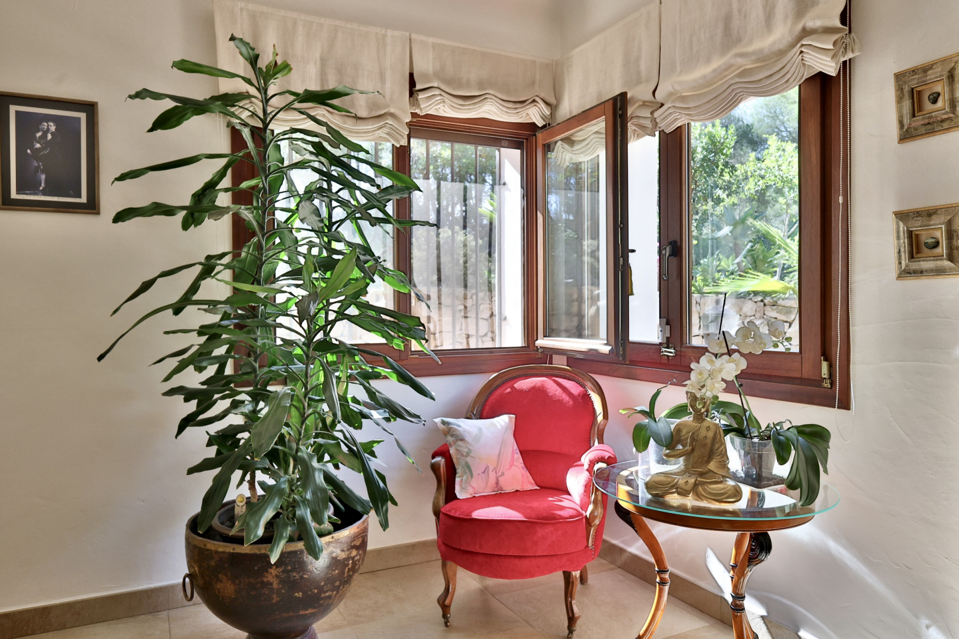 Rincón acogedor con ventanales de madera que ofrecen vistas al jardín, sillón rojo tapizado y una planta exuberante. Incluye mesa auxiliar con estatua de Buda y orquídea. Rincón acogedor con ventanales de madera que ofrecen vistas al jardín, sillón rojo tapizado y una planta exuberante. Incluye mesa auxiliar con estatua de Buda y orquídea.