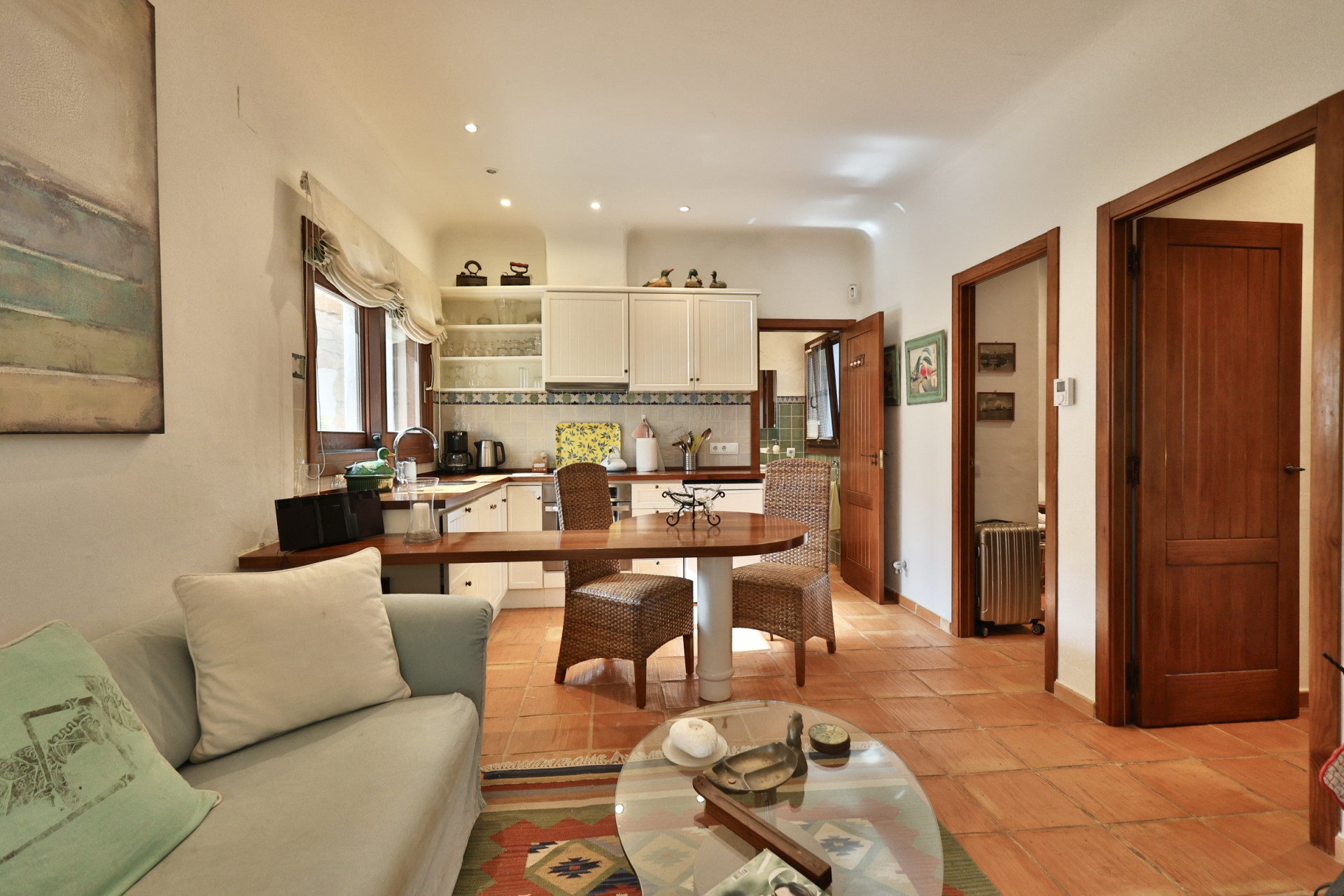 Salón-cocina de concepto abierto con suelo de terracota. La cocina equipada presenta muebles blancos, encimera de madera y barra de desayuno integrada con sillas de mimbre. Salón-cocina de concepto abierto con suelo de terracota. La cocina equipada presenta muebles blancos, encimera de madera y barra de desayuno integrada con sillas de mimbre.