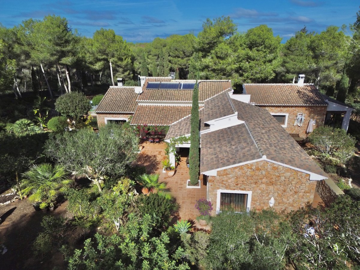 Vista aérea de la villa con fachada de piedra y tejado de teja, rodeada por un extenso jardín mediterráneo y pinos. Se aprecian paneles solares y una terraza de terracota. Vista aérea de la villa con fachada de piedra y tejado de teja, rodeada por un extenso jardín mediterráneo y pinos. Se aprecian paneles solares y una terraza de terracota.