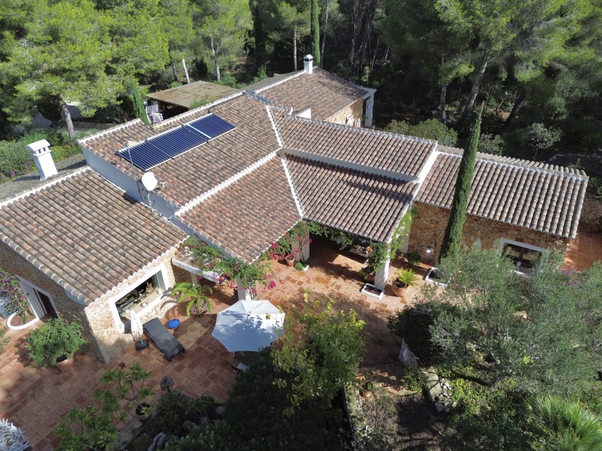 Vista aérea de la villa con tejados de teja, muros de piedra y una extensa terraza de terracota. Se aprecian paneles solares y una pérgola cubierta, rodeada de vegetación mediterránea. Vista aérea de la villa con tejados de teja, muros de piedra y una extensa terraza de terracota. Se aprecian paneles solares y una pérgola cubierta, rodeada de vegetación mediterránea.