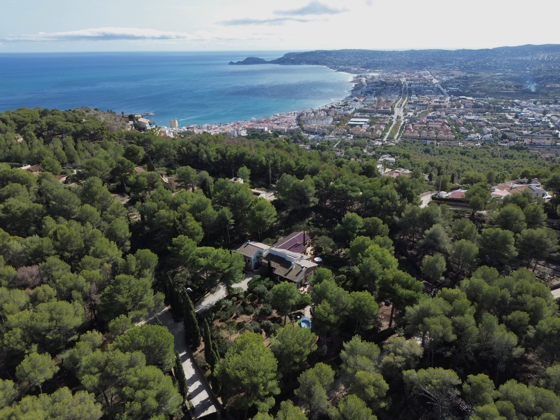 Vista aérea de la villa en una extensa parcela arbolada, con un camino privado y Jávea, su bahía y el mar Mediterráneo al fondo. Vista aérea de la villa en una extensa parcela arbolada, con un camino privado y Jávea, su bahía y el mar Mediterráneo al fondo.