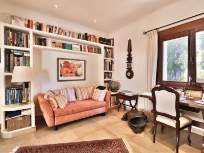 Acogedor estudio con estanterías empotradas llenas de libros, un sofá coral y un escritorio de madera junto a una ventana grande con vistas a la vegetación.