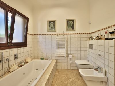 Baño principal con bañera de hidromasaje integrada, ventana de madera con cristal esmerilado y azulejos blancos con cenefa en tonos tierra.