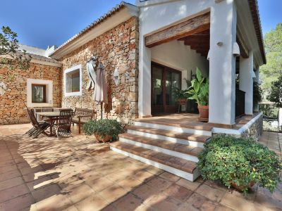 Patio exterior con paredes de piedra natural y suelo de terracota, equipado con un comedor al aire libre y un porche cubierto con vigas de madera.