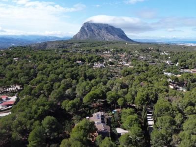 Vista aérea de la villa integrada en un denso bosque de pinos, con el Montgó y la costa de Jávea al fondo.