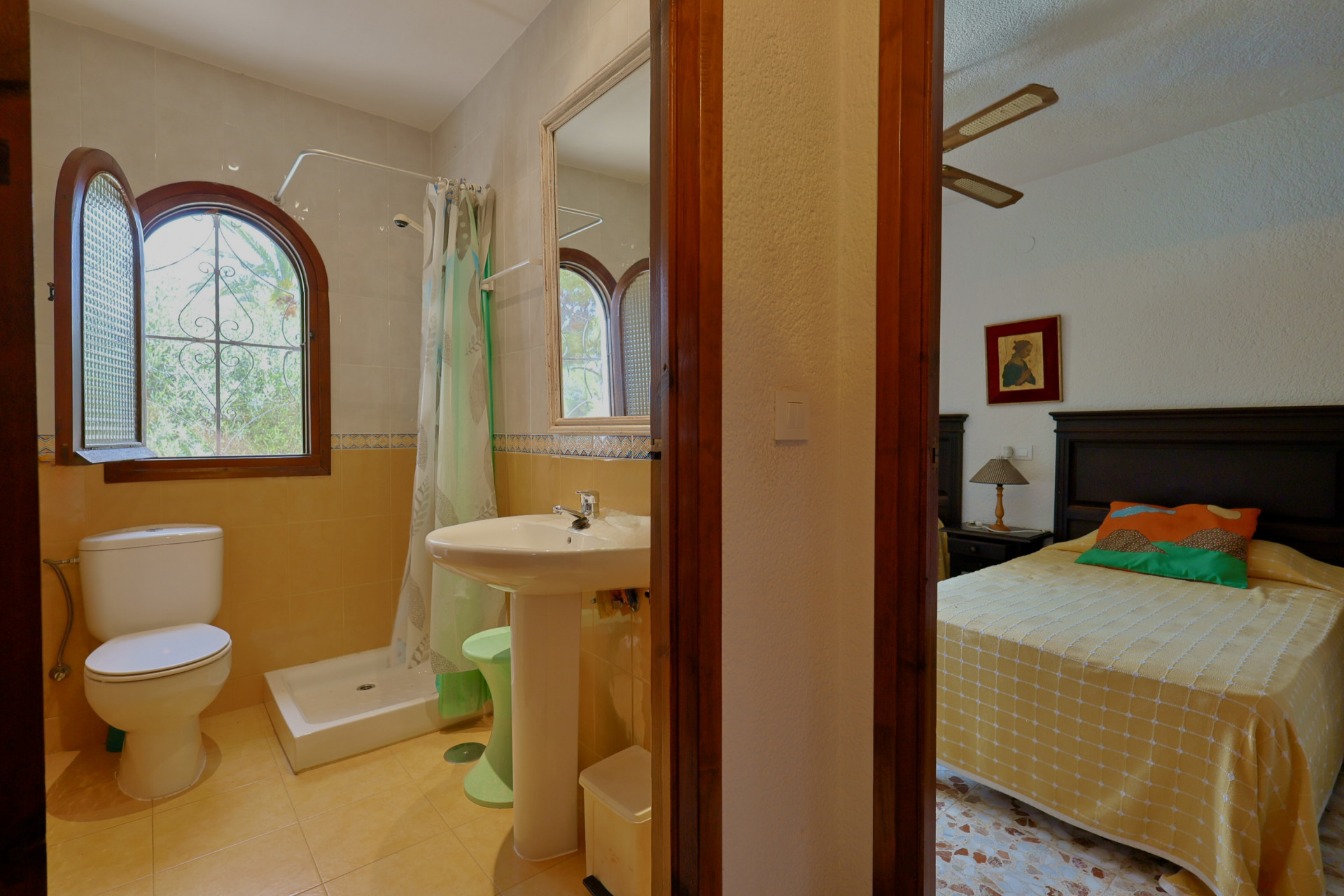 Baño con ducha, inodoro y lavabo de pedestal, destacando una ventana arqueada de madera con vistas a la vegetación. Se conecta visualmente con un dormitorio adyacente. Baño con ducha, inodoro y lavabo de pedestal, destacando una ventana arqueada de madera con vistas a la vegetación. Se conecta visualmente con un dormitorio adyacente.