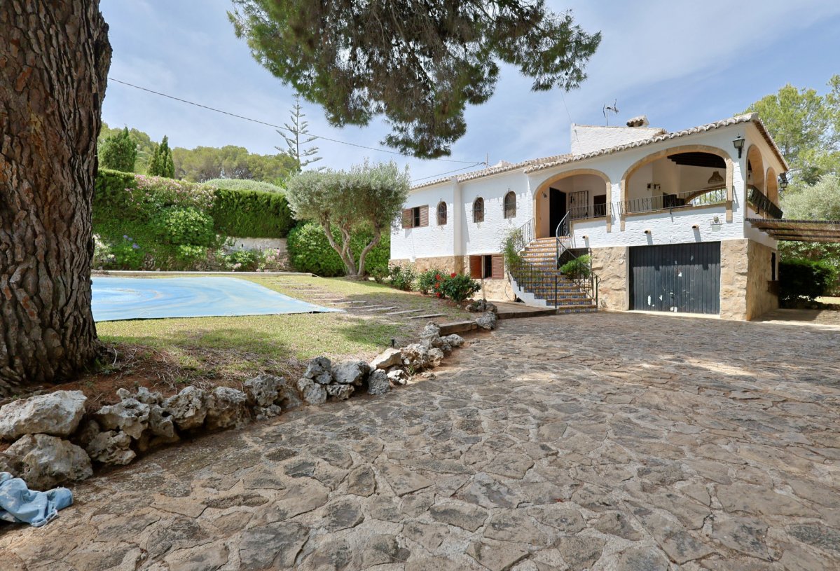 Exterior de la villa con amplia entrada empedrada, destacando la fachada blanca con arcos y la escalera principal. Se aprecia la zona de piscina cubierta y vegetación mediterránea. Exterior de la villa con amplia entrada empedrada, destacando la fachada blanca con arcos y la escalera principal. Se aprecia la zona de piscina cubierta y vegetación mediterránea.