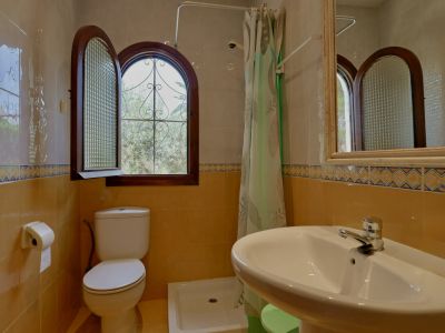 Baño con ventana de arco de madera, cristal texturizado y reja de hierro forjado. Azulejos bicolor con cenefa decorativa, inodoro y lavabo de cerámica blanca.