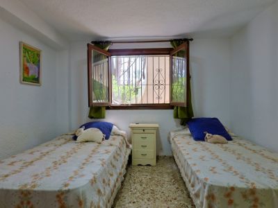 Dormitorio con dos camas individuales, mesita de noche, suelo de terrazo y ventana con rejas de seguridad y vistas a la vegetación.