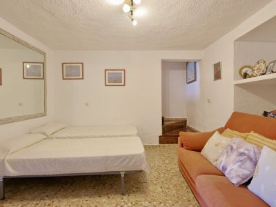 Sala polivalente con dos camas individuales, sofá naranja, suelo de terrazo y estanterías empotradas. Un gran espejo amplía visualmente el espacio.