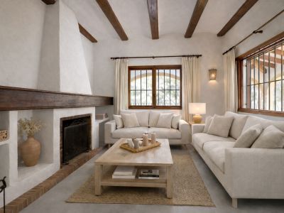 Salón con chimenea tradicional de estuco blanco y viga de madera oscura. Destacan las vigas vistas en el techo y los ventanales con marcos de madera y rejas.