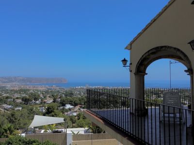 Terraza cubierta con vistas panorámicas al mar, la ciudad y el paisaje, enmarcada por un arco de piedra y barandilla de hierro.
