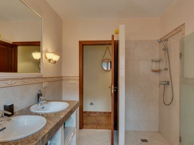 Baño principal con doble lavabo sobre encimera de granito, espejo enmarcado y ducha de obra con mampara de cristal, destacando los azulejos de tonos cálidos.