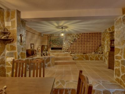Bodega rústica con paredes de piedra natural y suelo de baldosas de terracota. Destaca una vinoteca de obra y un nicho escalonado, con una lámpara central que proyecta un patrón único en el techo.