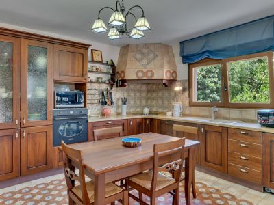 Cocina tradicional con armarios de madera oscura, salpicadero de azulejos con patrones intrincados y una mesa de comedor central. Luz natural entra por la ventana con vistas a la vegetación.