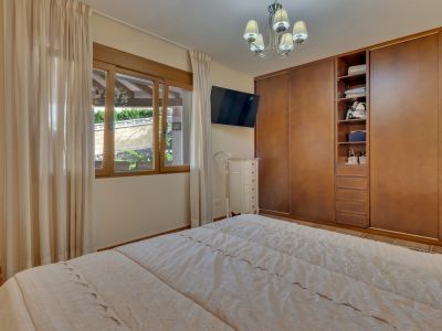 Dormitorio con cama doble, armarios empotrados de madera y ventana con vistas a un muro ajardinado. Incluye TV montada en pared y cómoda blanca.