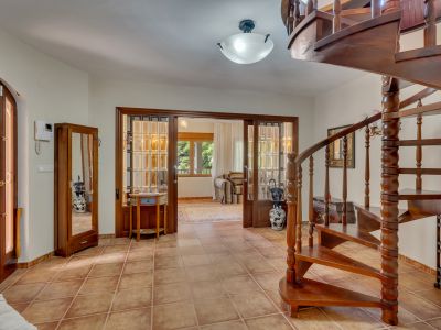 Entrada principal con escalera de caracol de madera oscura y suelo de baldosas de terracota. Puertas correderas de madera y cristal conectan con una estancia luminosa.