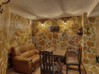 Espacio interior con paredes revestidas de piedra irregular y suelo de baldosas. Incluye un sofá de cuero, mesa rústica de madera y cálida iluminación de faroles.
