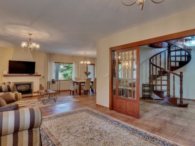 Salón-comedor abierto con chimenea y suelos de baldosas, conectando con una elegante escalera de caracol de madera a través de puertas correderas de cristal.