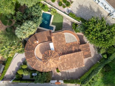 Vista aérea de la villa con techos de teja roja, piscina privada con diseño de brújula y exuberantes jardines mediterráneos.