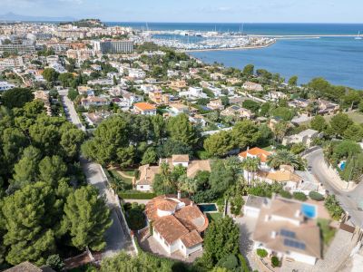 Vista aérea de la villa con tejado de teja roja y piscina privada, en una zona residencial verde de Dénia, con el puerto deportivo y el mar al fondo.