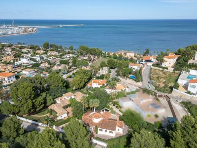 Vista aérea de la zona residencial de Dénia, mostrando villas, vegetación y el puerto deportivo junto al mar Mediterráneo.
