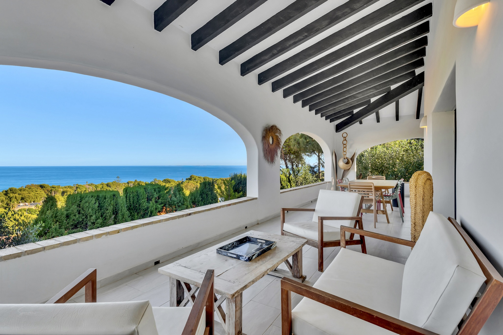 Terraza cubierta con vigas de madera oscura y suelo de baldosas blancas. Ofrece vistas panorámicas al mar a través de arcos, con mobiliario de exterior en madera. Terraza cubierta con vigas de madera oscura y suelo de baldosas blancas. Ofrece vistas panorámicas al mar a través de arcos, con mobiliario de exterior en madera.