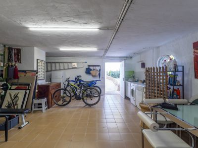 Amplio cuarto de servicio con lavadora, secadora, fregadero y estanterías. Cuenta con suelo de baldosas, iluminación fluorescente y acceso directo al exterior.