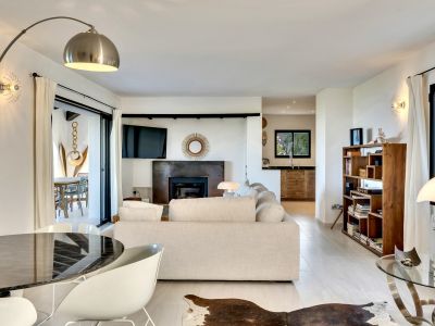 Amplio salón con sofá claro, chimenea de diseño y televisor integrado. Puertas correderas conectan con la terraza exterior. Mesa de comedor moderna y estantería de madera complementan el espacio.