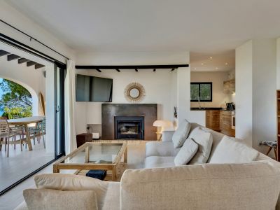 Amplio salón con sofá seccional y chimenea moderna, conectando directamente con una terraza exterior que ofrece vistas al mar y área de comedor.