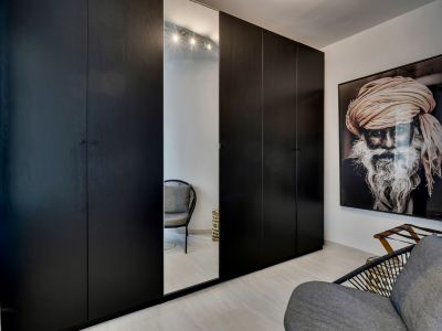 Armarios empotrados oscuros con acabado de madera, incluyendo una puerta espejada que refleja una silla moderna. Suelos claros y una gran obra de arte en la pared.