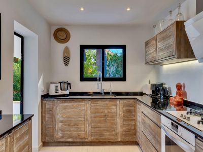 Cocina equipada con gabinetes de madera rústica, encimeras negras y ventana con vistas al jardín. Incluye electrodomésticos modernos y fregadero doble.