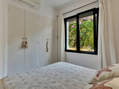 Dormitorio con armarios empotrados blancos, unidad de aire acondicionado y ventana que enmarca una vista vibrante de buganvillas rosadas.