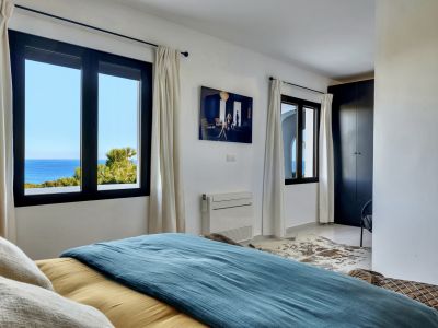 Dormitorio luminoso con vistas directas al mar Mediterráneo a través de ventanas de marco oscuro. Incluye armario empotrado, aire acondicionado y decoración moderna.