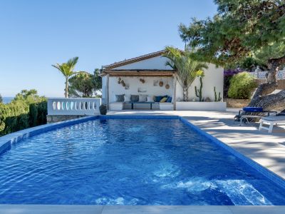 Piscina privada de mosaico azul con vistas al mar, flanqueada por una pérgola de madera y una zona de estar exterior.