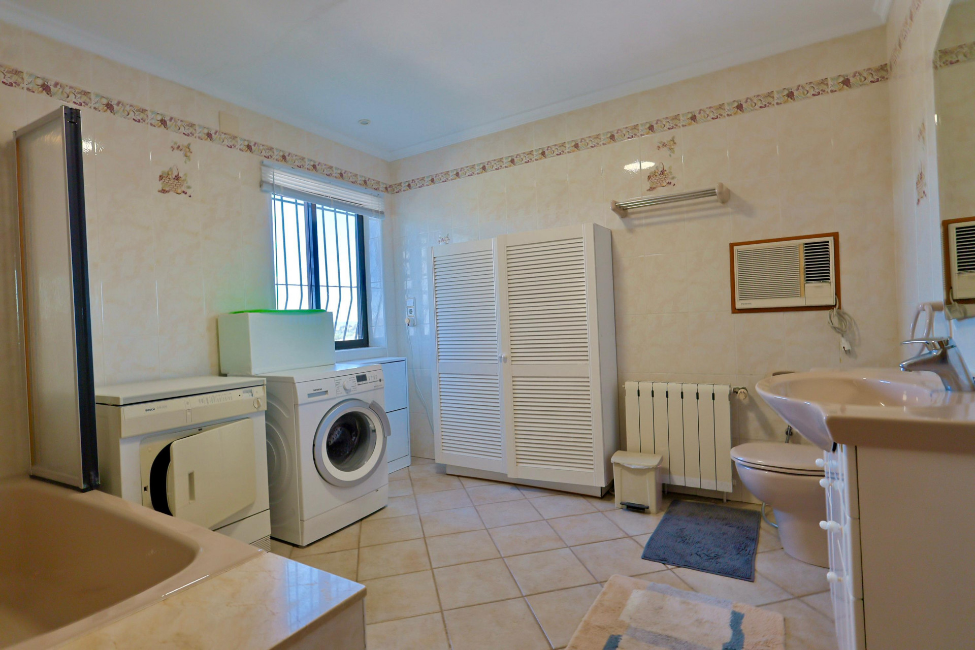 Cuarto de baño funcional con lavadora, secadora y amplio armario de persianas blancas.