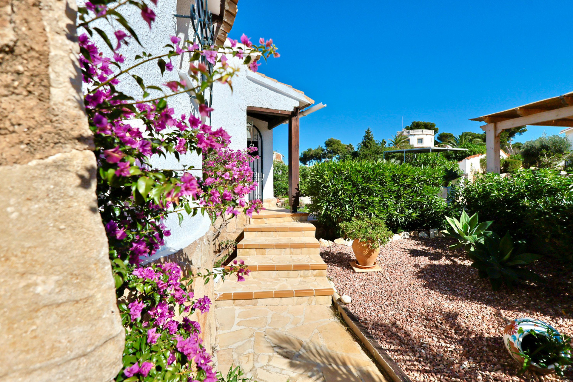 Entrada a la villa con buganvillas fucsias y jardín de grava.